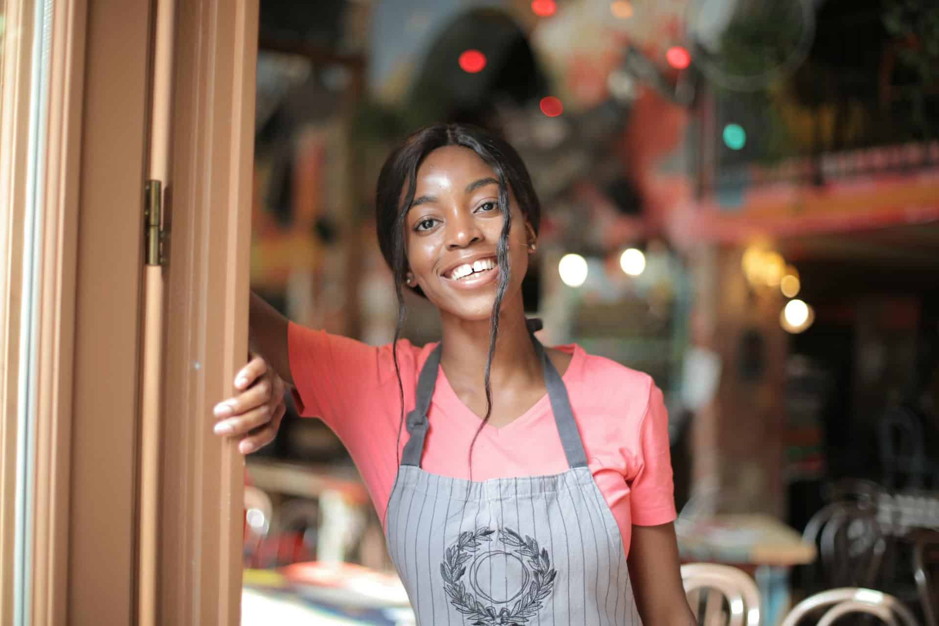 Cheerful woman in apron smiling while standing in a vibrant indoor setting.